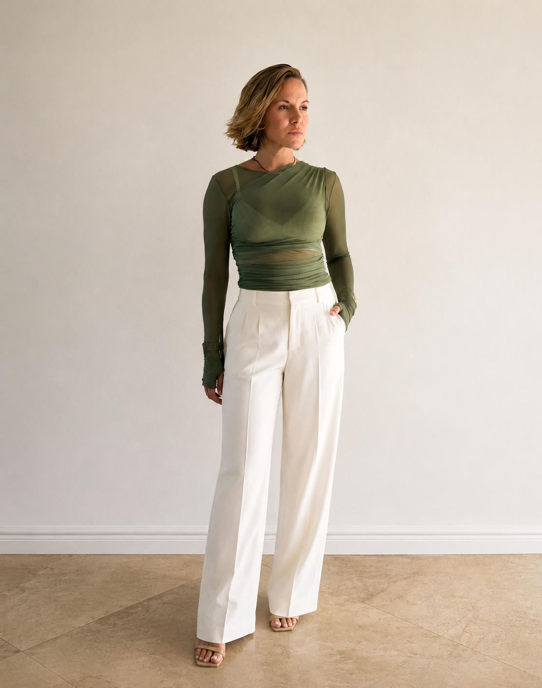 Moony Koch in a green mesh top and white wide-leg trousers against a soft white wall