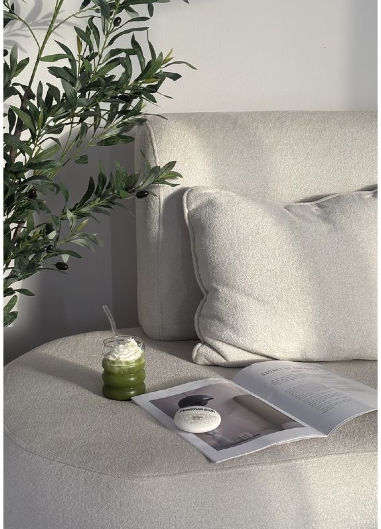 Matcha and an open magazine on a cream bouclé sofa beside an olive tree